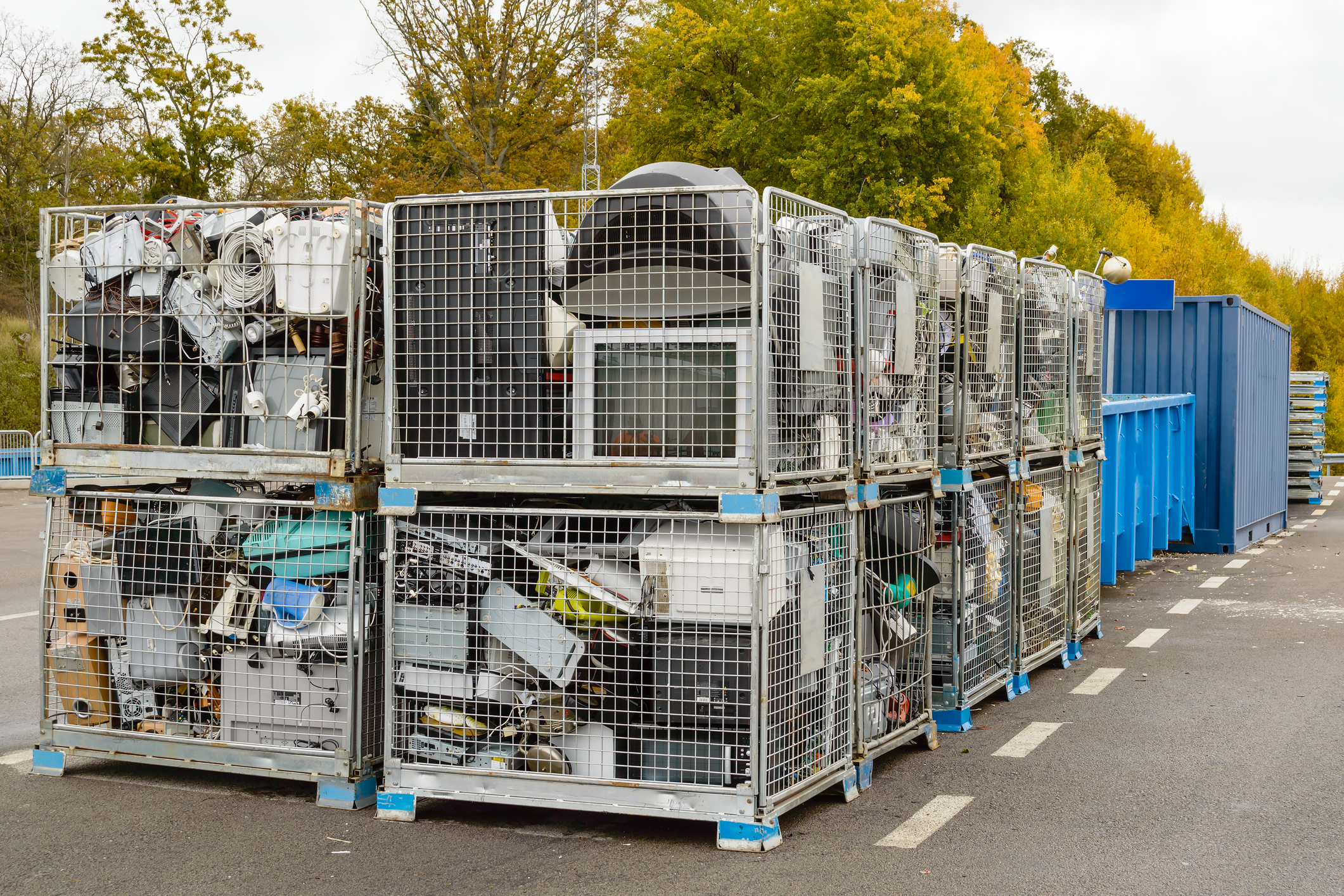 Netted bins full of discarded electronics waste waiting to be transported to the recycle plant for further processing. Blue containers in background. Waste Separation